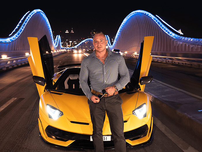 Elegant man posing next to a yellow sports car with open doors, on a bridge illuminated at night